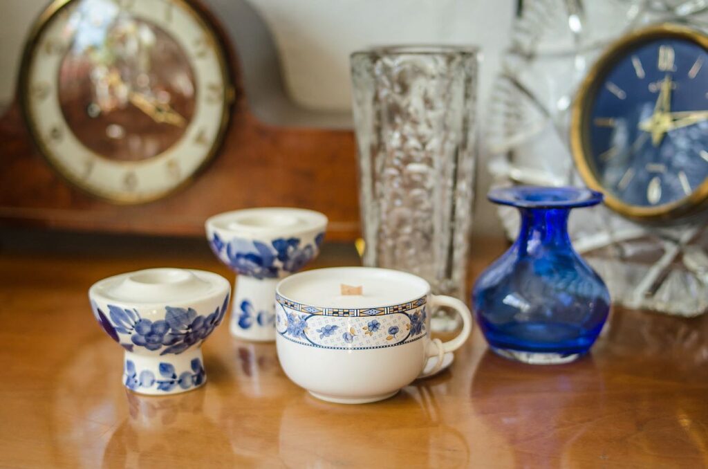 świeca w vintage filiżance na kawę z niebieskim motywem kwiatowym, obok inne naczynka vintage biało niebieskie stojące na drewnianym stole