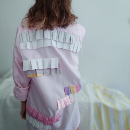 dziewczyna stojąca tyłem w koszuli różowej z kolorowymi falbankami. koszula jest rozmiaru oversize, z recyklingu